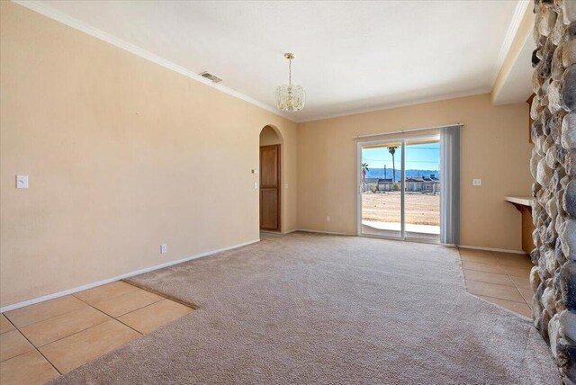 carpeted empty room featuring a stone fireplace, crown molding, and an inviting chandelier