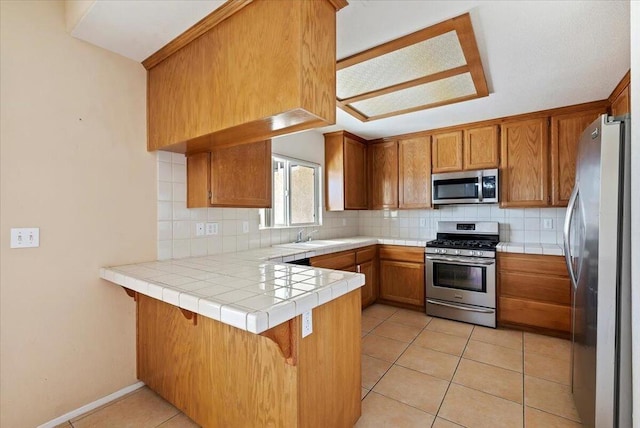 kitchen featuring tile countertops, backsplash, light tile patterned floors, kitchen peninsula, and stainless steel appliances