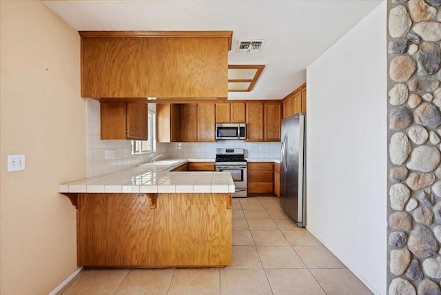 kitchen featuring kitchen peninsula, appliances with stainless steel finishes, backsplash, sink, and tile countertops