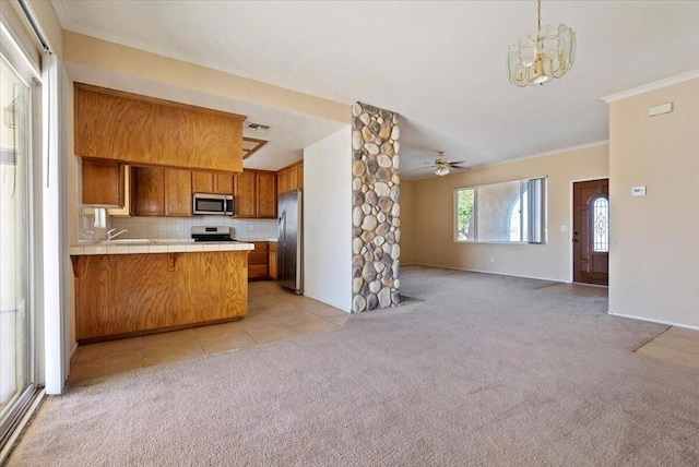 kitchen with kitchen peninsula, appliances with stainless steel finishes, backsplash, ceiling fan with notable chandelier, and crown molding