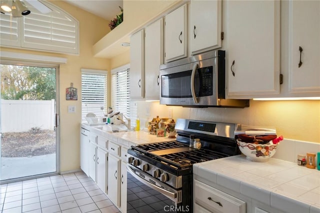 kitchen with white cabinets, tile counters, light tile patterned floors, and appliances with stainless steel finishes