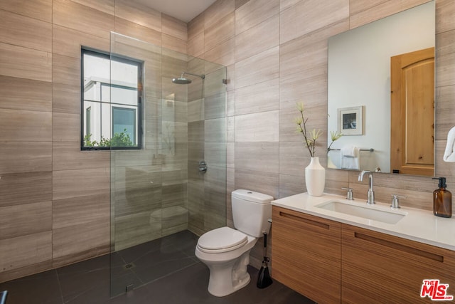 bathroom featuring tile patterned flooring, tiled shower, toilet, vanity, and tile walls