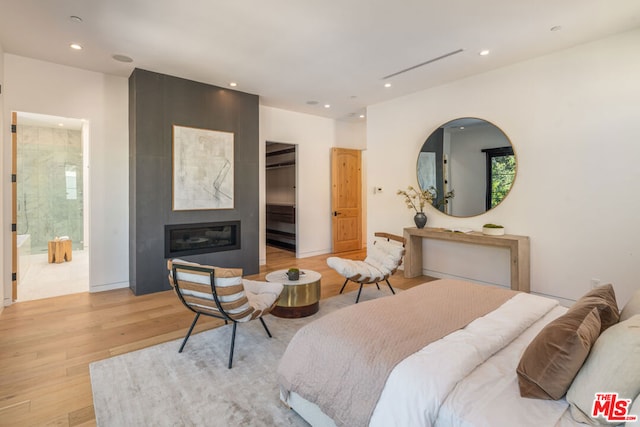 bedroom with ensuite bath, a large fireplace, and light hardwood / wood-style floors