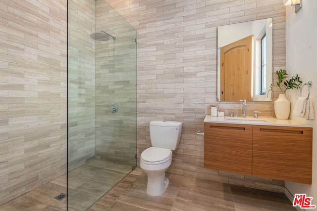 bathroom featuring a tile shower, vanity, toilet, and tile walls