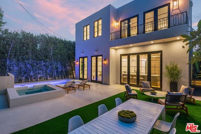 back house at dusk with a swimming pool with hot tub, a balcony, a patio, and french doors