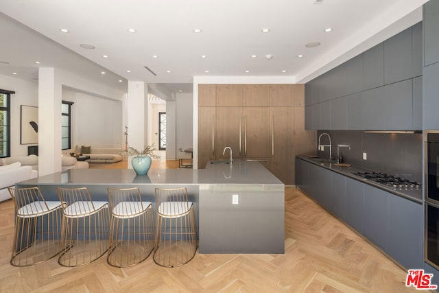 kitchen with sink, decorative backsplash, a large island, stainless steel gas cooktop, and light parquet flooring