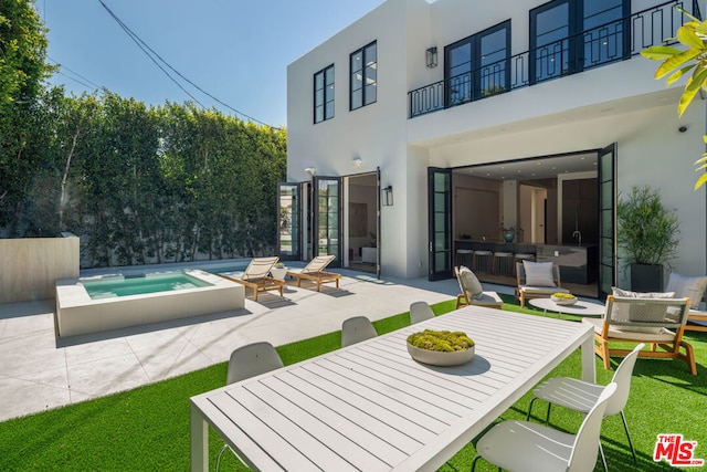 rear view of house with a swimming pool with hot tub, a balcony, and a patio area