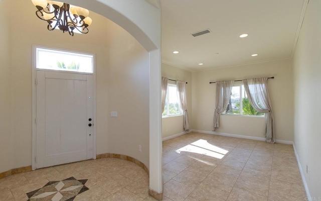 foyer entrance with a wealth of natural light, light tile patterned floors, ornamental molding, and an inviting chandelier