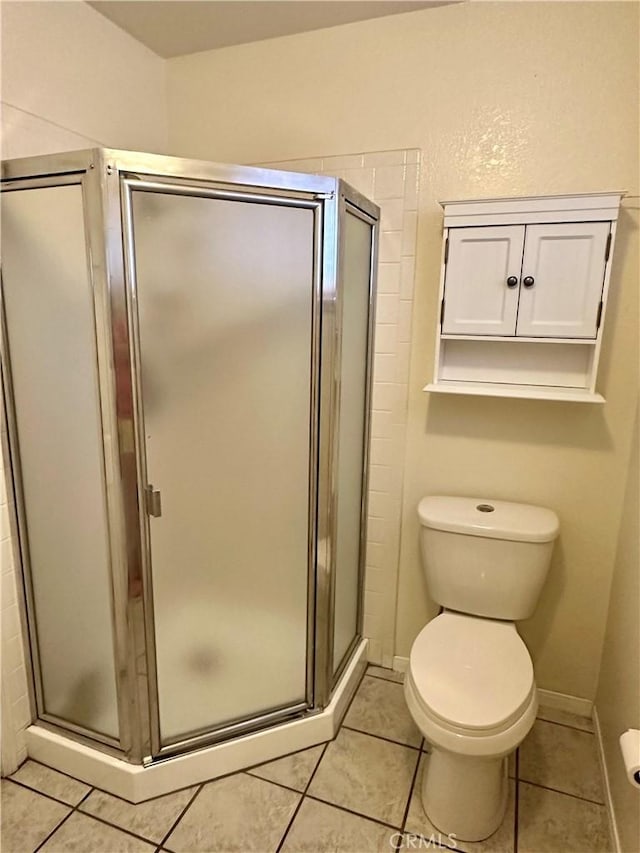 bathroom with tile patterned floors, toilet, and a shower with shower door