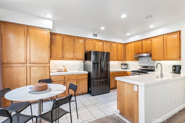 197 Lydia Ln, Corona, CA 92882 - kitchen featuring black refrigerator with ice dispenser, stainless steel range with gas stovetop, under cabinet range hood, a peninsula, and brown cabinetry