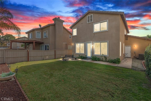 back house at dusk with a patio, central AC unit, and a lawn