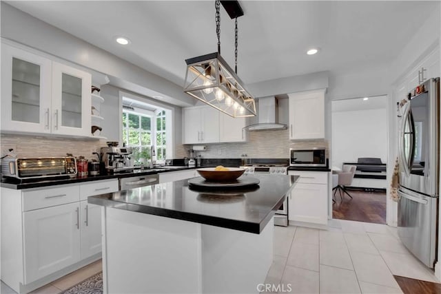 kitchen with stainless steel appliances, wall chimney range hood, a kitchen island, pendant lighting, and white cabinets