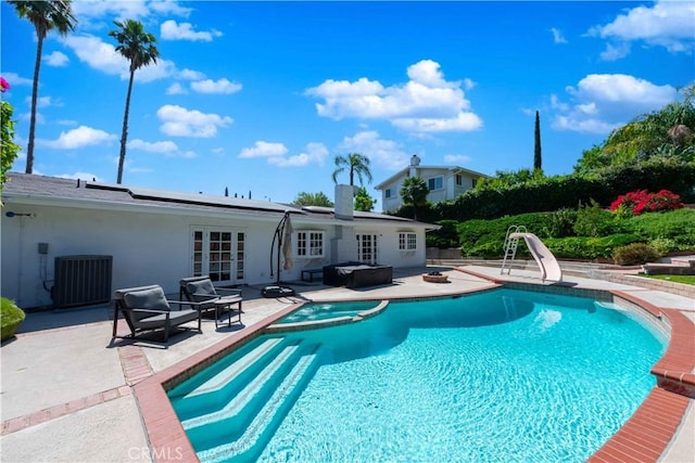 view of pool with a water slide, french doors, cooling unit, an in ground hot tub, and a patio area