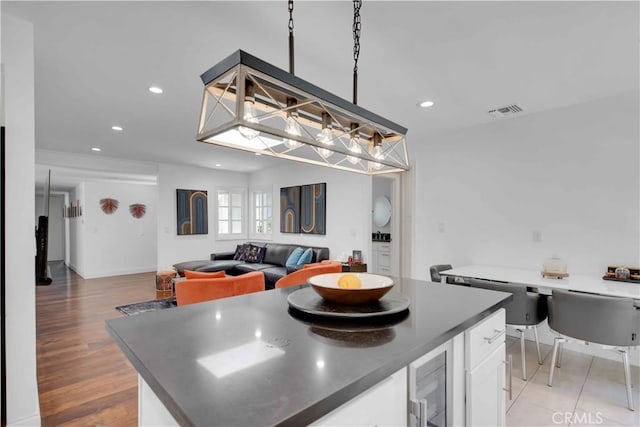 kitchen with beverage cooler, light hardwood / wood-style flooring, white cabinets, a kitchen island, and hanging light fixtures