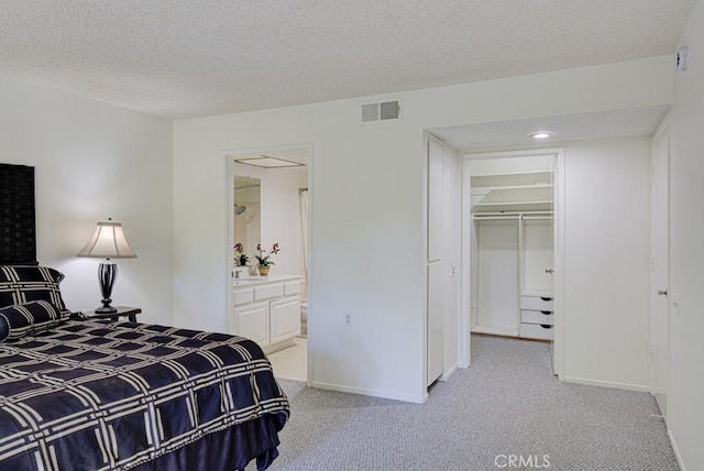 bedroom with a walk in closet, a textured ceiling, light carpet, and a closet