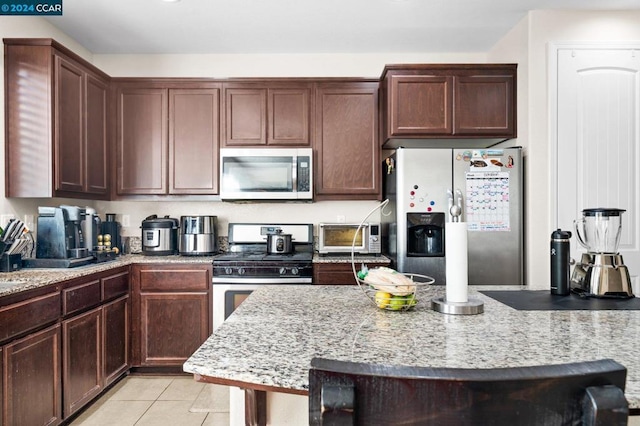 kitchen featuring light tile patterned floors, stainless steel appliances, light stone counters, and dark brown cabinets