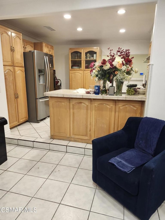 kitchen featuring crown molding, light tile patterned flooring, tile countertops, and stainless steel fridge