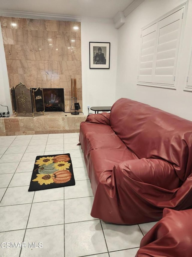 tiled living room featuring crown molding and a stone fireplace