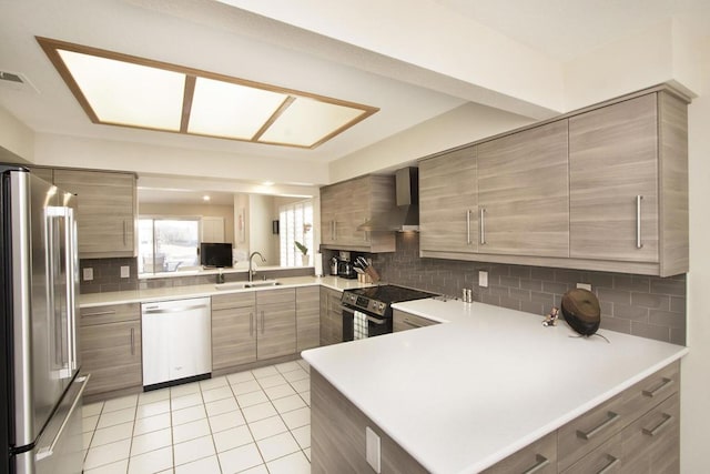 kitchen with kitchen peninsula, backsplash, stainless steel appliances, wall chimney range hood, and sink