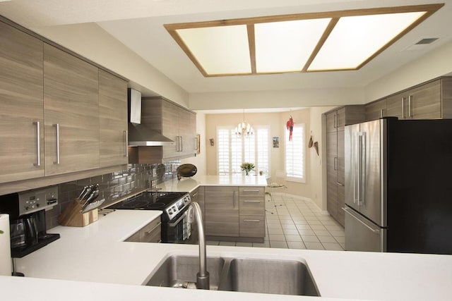 kitchen with wall chimney range hood, sink, a notable chandelier, kitchen peninsula, and stainless steel appliances