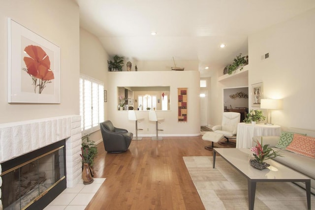 living room featuring a brick fireplace, lofted ceiling, and light wood-type flooring