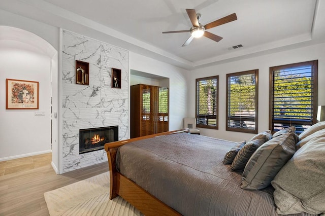 bedroom featuring ceiling fan, a large fireplace, and light hardwood / wood-style flooring