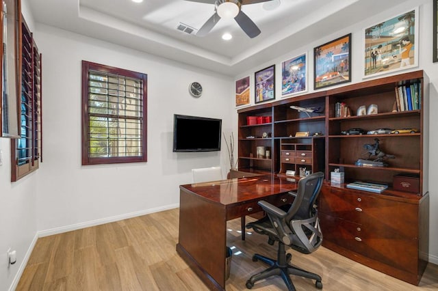 office area featuring ceiling fan, light wood-type flooring, and a tray ceiling