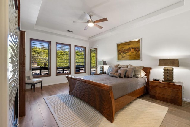 bedroom with hardwood / wood-style flooring, ceiling fan, and a tray ceiling