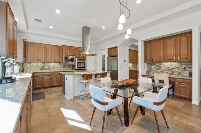 kitchen with pendant lighting, a kitchen island, light stone counters, island exhaust hood, and stainless steel appliances