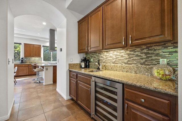 bar featuring light stone countertops, tasteful backsplash, beverage cooler, sink, and exhaust hood