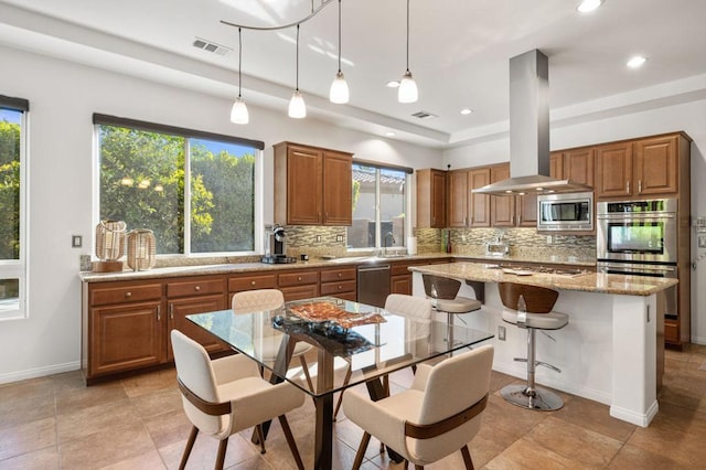 kitchen with light stone countertops, a center island, island exhaust hood, decorative light fixtures, and appliances with stainless steel finishes