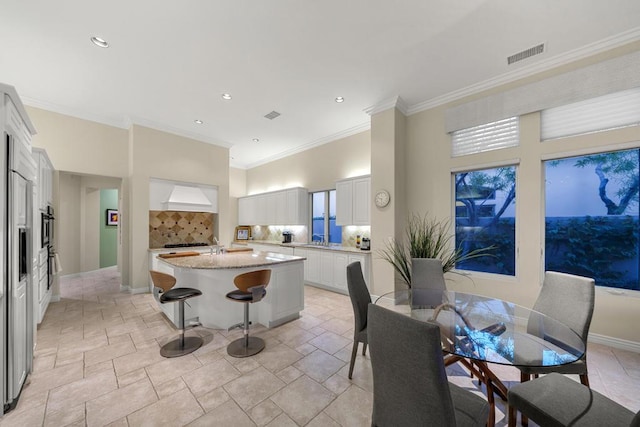 kitchen featuring white cabinetry, a center island, light stone countertops, backsplash, and ornamental molding