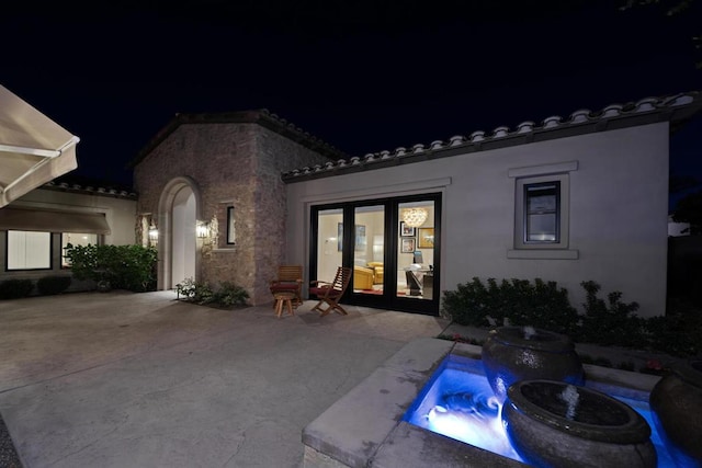 back house at night featuring a patio area and french doors