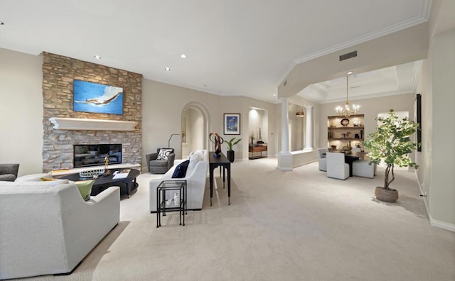 carpeted living room with an inviting chandelier, a stone fireplace, crown molding, a tray ceiling, and decorative columns