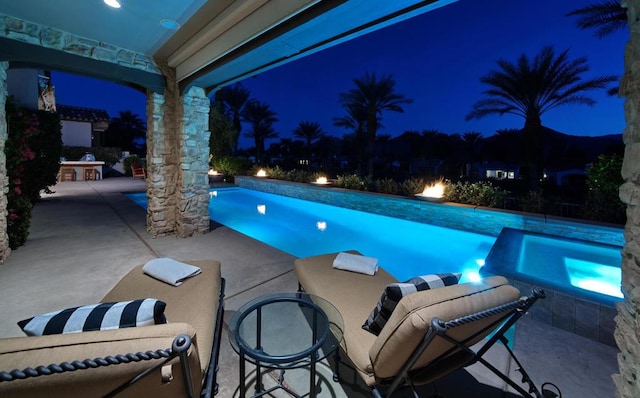 pool at twilight featuring an in ground hot tub and a patio