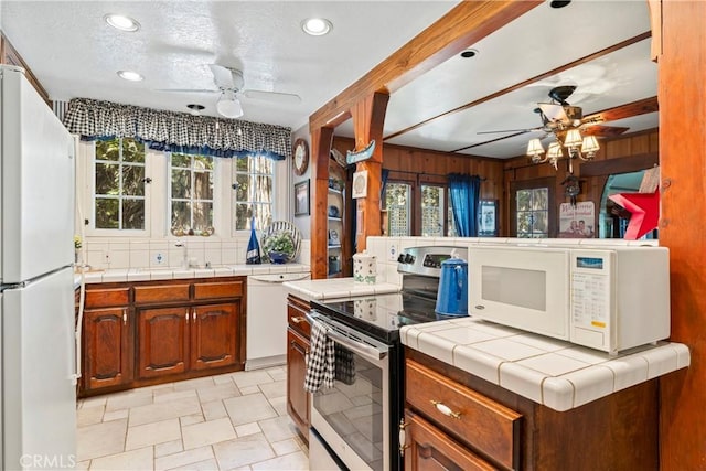 kitchen featuring a textured ceiling, white appliances, wooden walls, sink, and tile counters