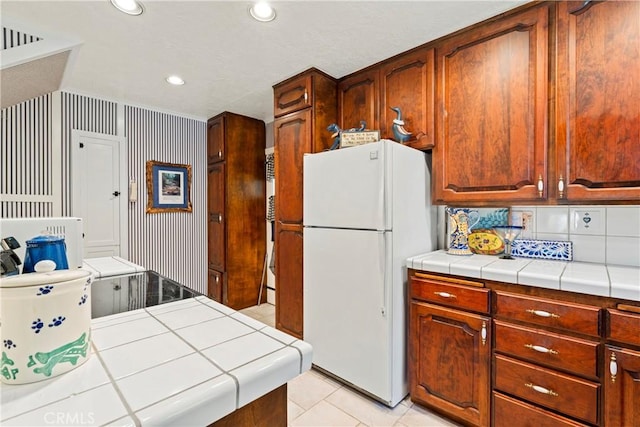 kitchen with tile counters, white fridge, light tile patterned floors, and tasteful backsplash