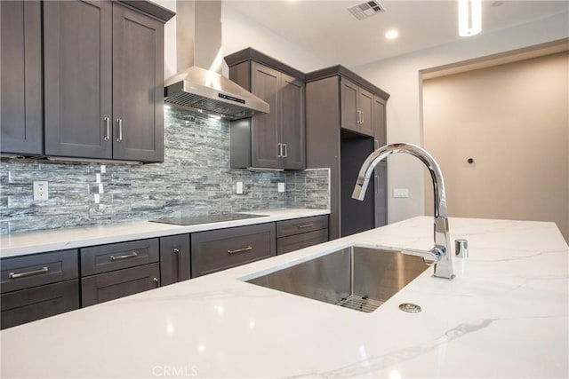 kitchen featuring light stone countertops, black electric stovetop, backsplash, wall chimney exhaust hood, and sink