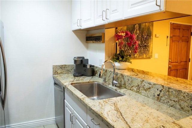 kitchen featuring white cabinetry, sink, stainless steel dishwasher, and light stone counters