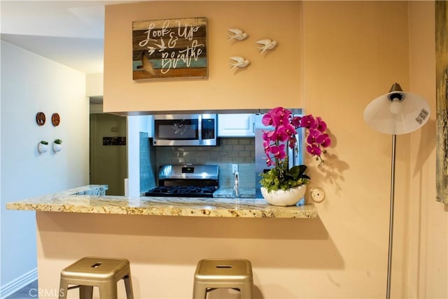 18645 Hatteras St Unit 186, Tarzana, CA 91356 - kitchen with appliances with stainless steel finishes, decorative backsplash, a breakfast bar, a peninsula, and light stone counters