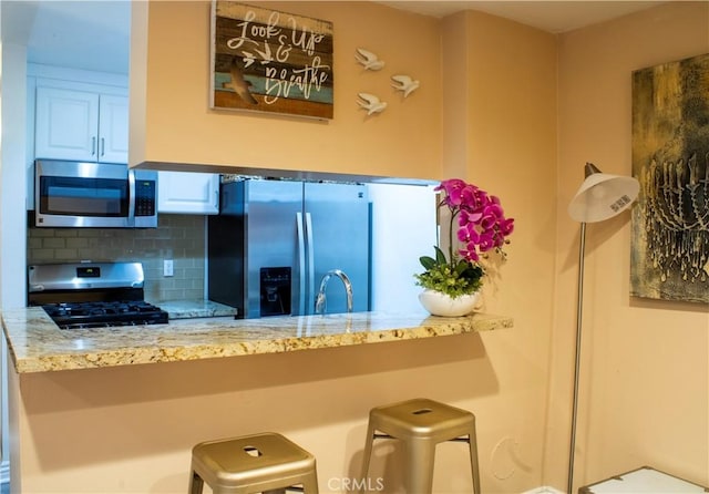 kitchen featuring light stone countertops, white cabinetry, backsplash, a kitchen bar, and appliances with stainless steel finishes