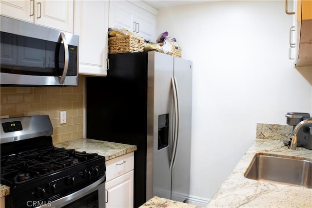 kitchen featuring light stone countertops, appliances with stainless steel finishes, backsplash, sink, and white cabinets