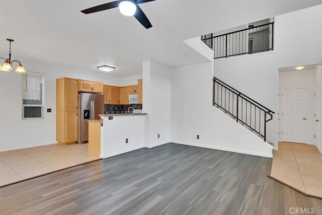 unfurnished living room with ceiling fan with notable chandelier and light wood-type flooring