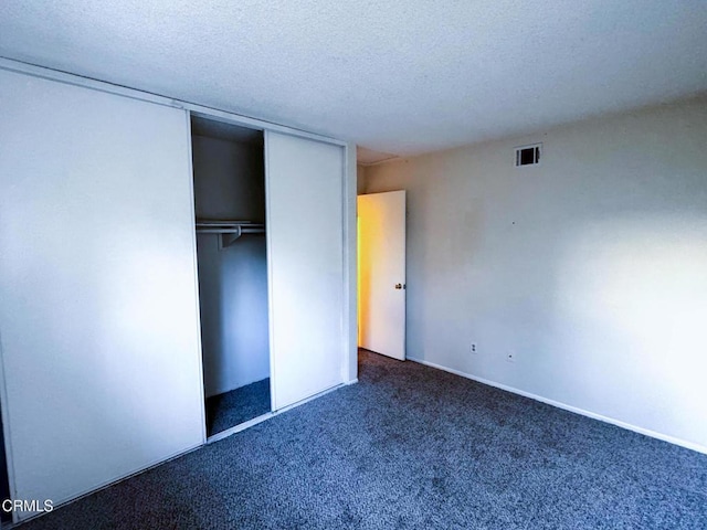 unfurnished bedroom featuring dark colored carpet, a textured ceiling, and a closet