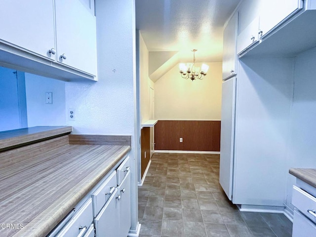 kitchen with pendant lighting, wood walls, white cabinetry, and an inviting chandelier