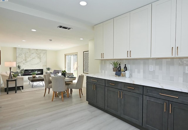 kitchen with light stone counters, light hardwood / wood-style flooring, backsplash, white cabinets, and a fireplace