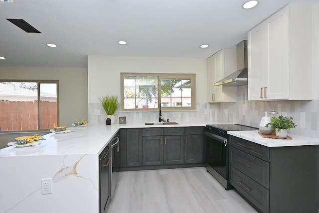 kitchen featuring sink, white cabinetry, light stone counters, wall chimney exhaust hood, and range with electric stovetop