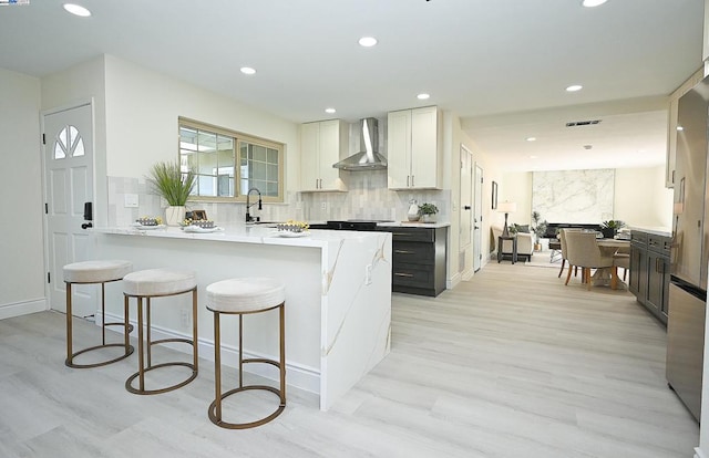 kitchen featuring white cabinets, wall chimney range hood, light hardwood / wood-style floors, and light stone countertops