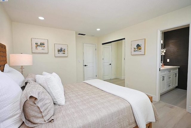 bedroom with connected bathroom and light hardwood / wood-style flooring