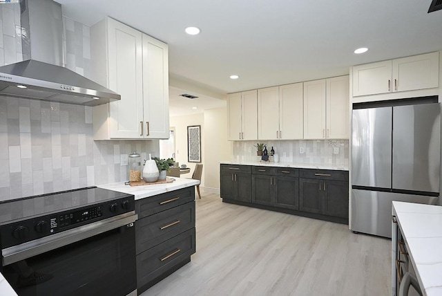 kitchen with white cabinetry, tasteful backsplash, electric stove, stainless steel fridge, and wall chimney range hood